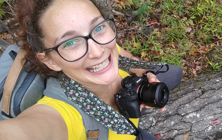 la photographe Aurore Degaigne, photographe de portraits corporatifs lifestyle à Montréal, en t-shirt jaune, qui s'est photographiée en selfie pendant une séance photo automnale, assise sur un tronc d'arbre